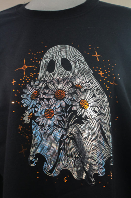 A close-up of a black t-shirt featuring a large, rhinestone-embellished graphic of a ghost holding a bouquet of white daisies with orange centers, surrounded by small orange stars.