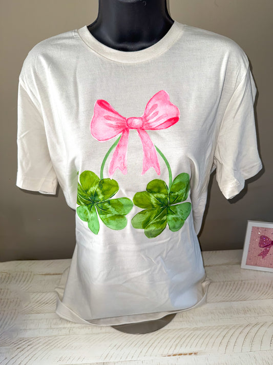 A vintage white unisex jersey t-shirt with a pink bow and green shamrock graphics on the front.