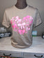 A beige T-shirt with a graphic of pink bows arranged in a heart shape on the front.
