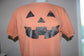 An orange short-sleeve t-shirt displayed on a mannequin torso, featuring a large black distressed jack-o'-lantern face graphic on the front.