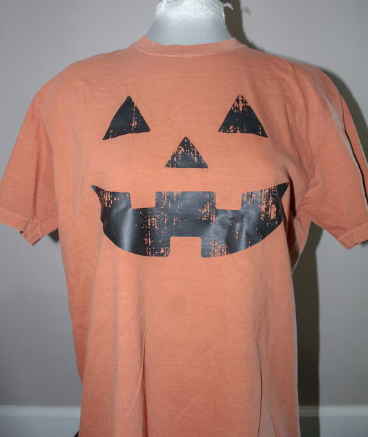An orange short-sleeve t-shirt displayed on a mannequin torso, featuring a large black distressed jack-o'-lantern face graphic on the front.