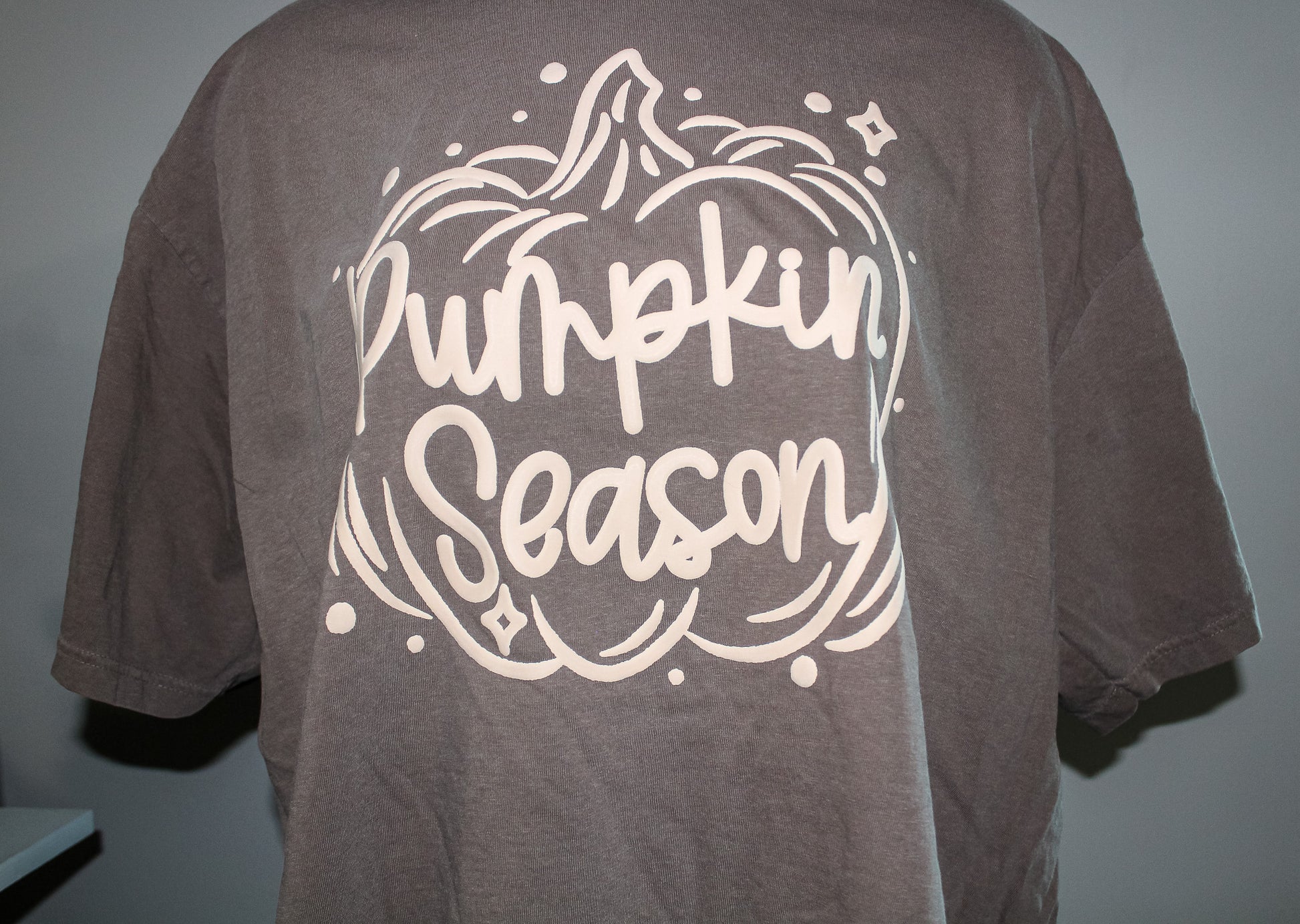 A faded brown short-sleeve t-shirt featuring a large white graphic on the back with the words 'Pumpkin Season' inside a pumpkin outline.