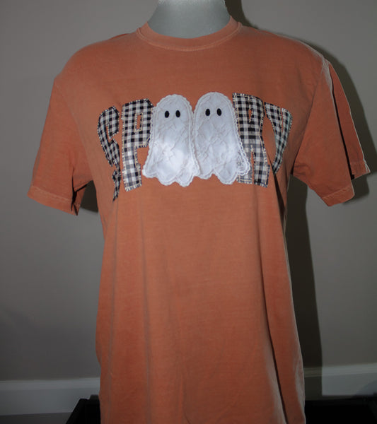 An orange short-sleeve t-shirt displayed on a mannequin torso, featuring a 'SPOIL' graphic across the chest with two white lace ghosts and black-and-white gingham patterned letters.